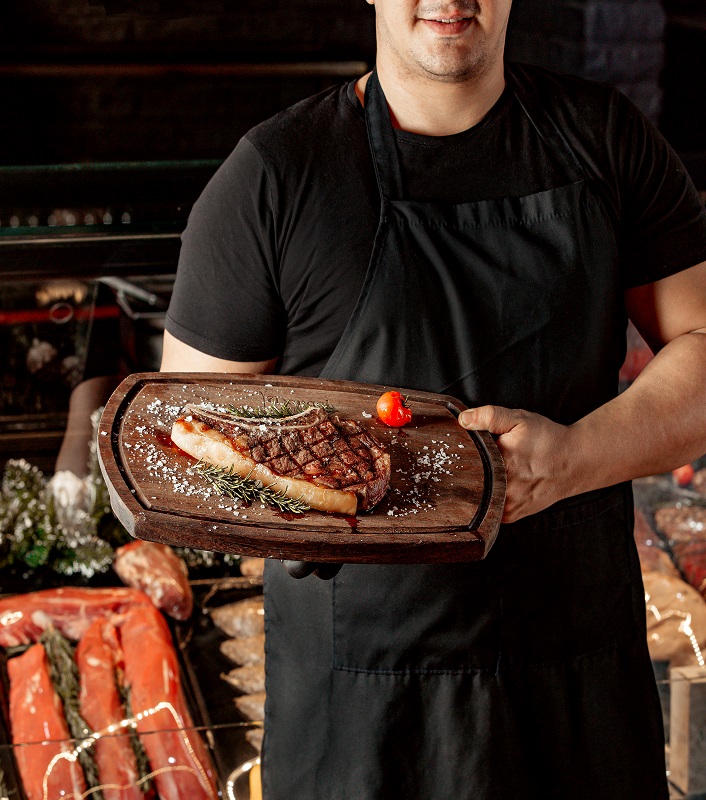 Homem mostrando um corte de carne de churrasco premium de pé.