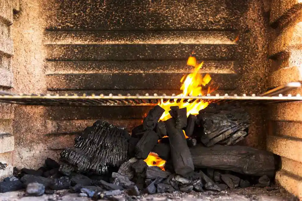 Imagem de uma churrasqueira vazia, com alguns pedaços de carvão pegando fogo.